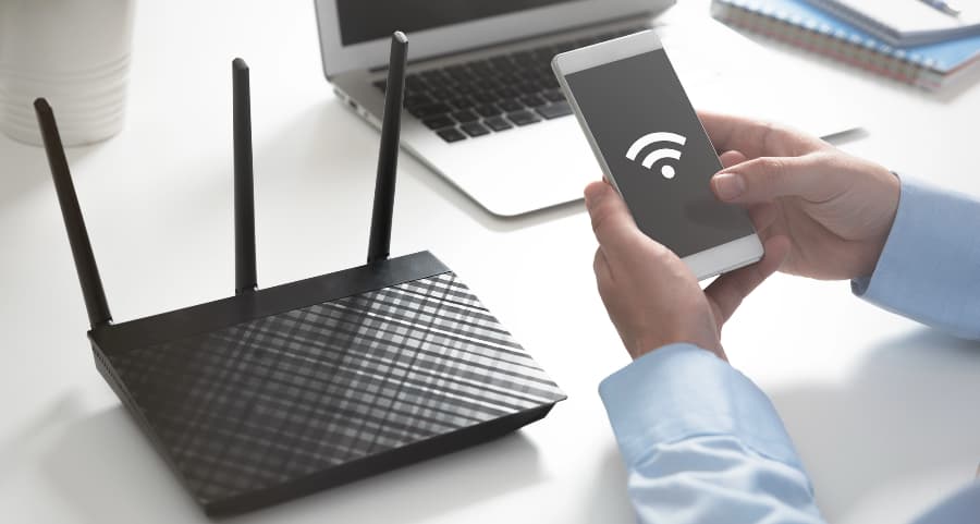 Man holding a cell phone at a desk near a wireless router.